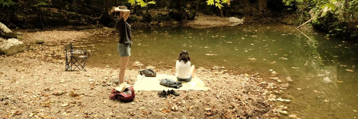 Two people relax by a quiet riverside surrounded by autumn leaves.